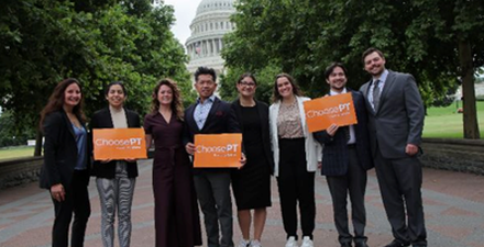 Group of eight advocates holding orange ‘ChoosePT’ signs outdoors, with trees and the U.S. Capitol building visible in the background.