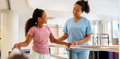 Physical therapist assists a child walking between parallel bars.