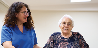 A PT assists an older woman walking with handrails