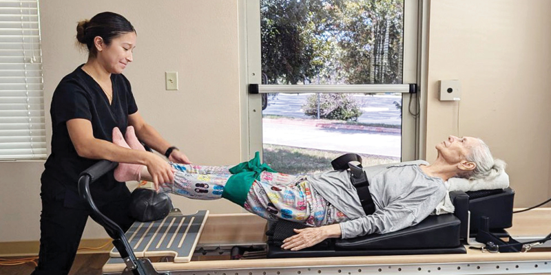 A PT guides a woman on a Pilates reformer